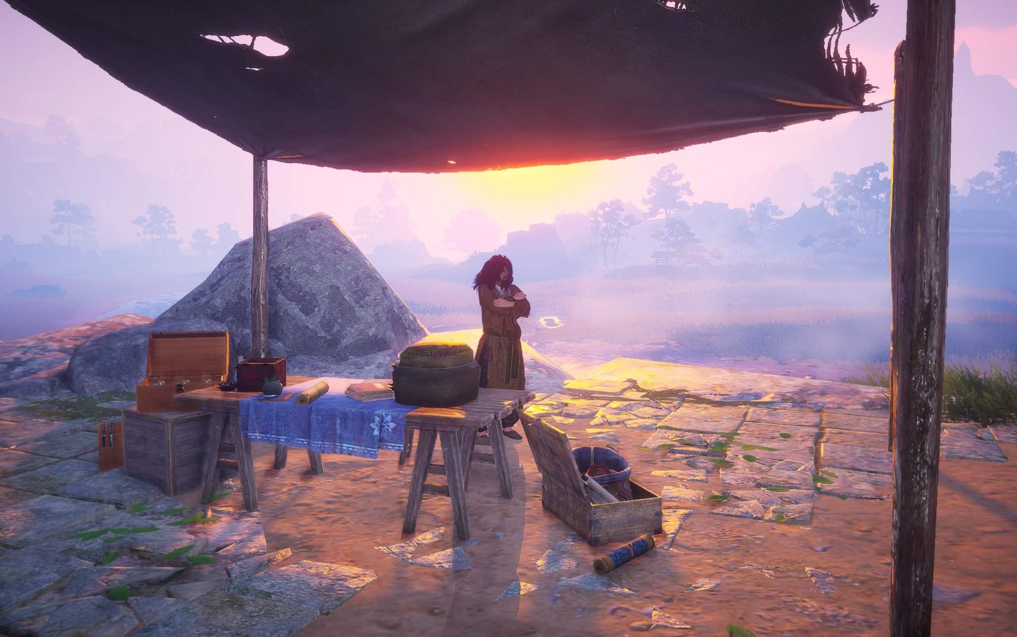 A person with long hair stands with arms crossed under a rustic shelter at sunset, overlooking a misty landscape.